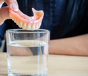 a person putting their dentures in a cup of water