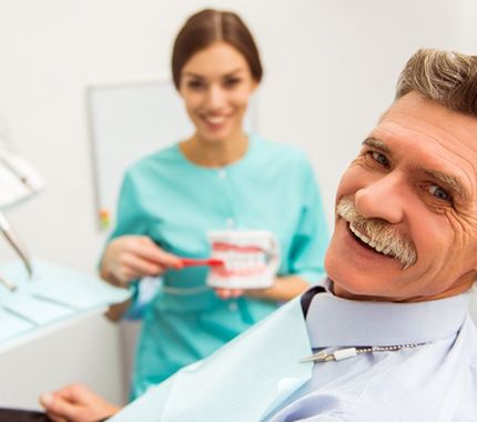 man smiling while reclining in dental examination chair after getting dentures