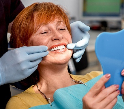 Older woman in dental chair looking at smile in mirror