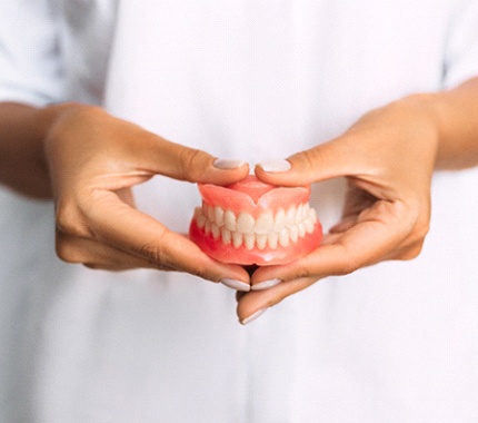 A dental professional using both hands to hold a full set of dentures