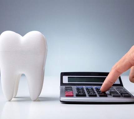 A person plugging in numbers on a calculator that is sitting next to an enlarged model of a tooth