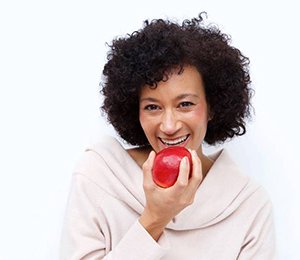 Woman with dental implants in Hillsboro eating an apple