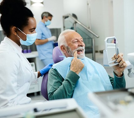 A senior man admiring his new dentures alongside his dentist
