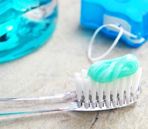 Close-up of toothbrush with toothpaste, next to floss and mouthwash