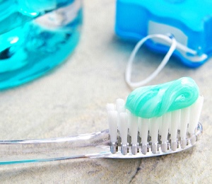 Close-up of toothbrush with toothpaste, next to floss and mouthwash