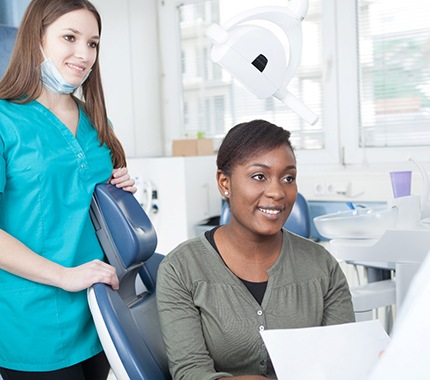 Dental assistant standing next to a female patient as the dentist discusses the cost of immediate dentures