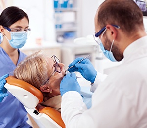A dentist and dental assistant examine a patient’s mouth to determine if they are eligible for dental implants