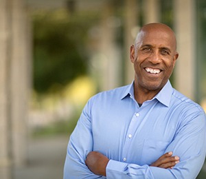 A middle-aged man wearing a blue button-down shirt stands outside and smiles after learning he’s eligible to receive dental implants