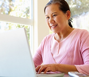 An older woman sitting at her laptop looking at alternative ways to pay for her dental implant treatment