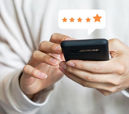 A person holding a cell phone and reading online reviews about a particular implant dentist