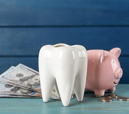 A ceramic tooth, a piggy bank, and money on a blue table