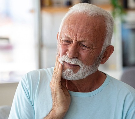 Bearded man in light blue shirt rubbing jaw in pain