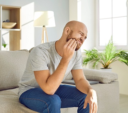 Man sitting on couch rubbing jaw due to discomfort