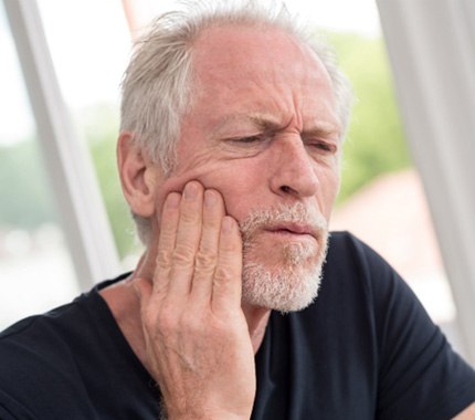 Old man who needs TMJ treatment in Hillsboro holding jaw