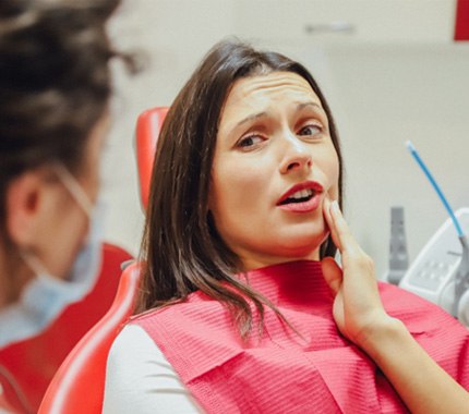 Woman with TMJ pain touching her jaw at dentist office 