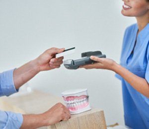 Dental receptionist smiling while taking payment from patient