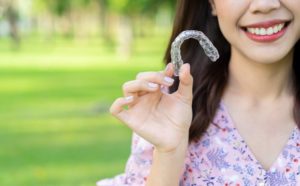smiling woman holding Invisalign outside