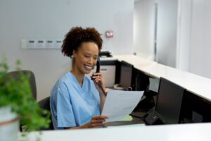 a smiling woman holding a piece of paper and talking on the phone with a patient
